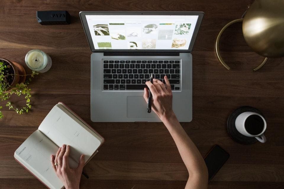 Vue de dessus d'un bureau : ordinateur portable, carnet ouvert et mains au travail