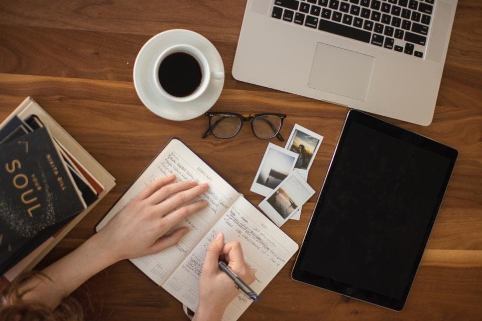 Mains qui prennent des notes dans un carnet, à côté d'un ordinateur portable et d'une tasse de café